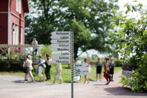 Kyltti jossa hääpaikan suuntaviittoja, taustalla Calliolan pihaa ja vieraita.